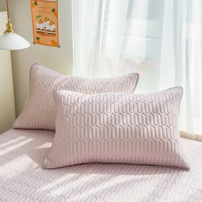 Soft blush pink quilted pillowcases with a geometric pattern complementing a quilted pink bed skirt set with silver trim