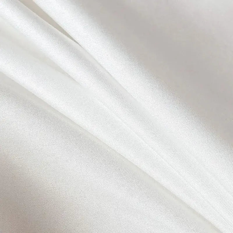 White satin fabric with smooth glossy finish and subtle woven texture on quilted tan duvet cover set for soft bedding