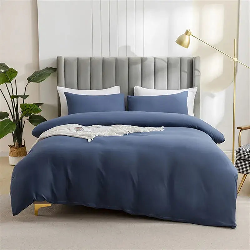 Navy blue satin duvet cover set with matching pillowcases and a white textured throw on a quilted tan duvet cover set bed