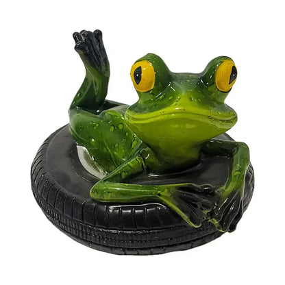 A glossy green frog figurine with bright yellow eyes lounges on a black tire in decorbites garden water floating decor
