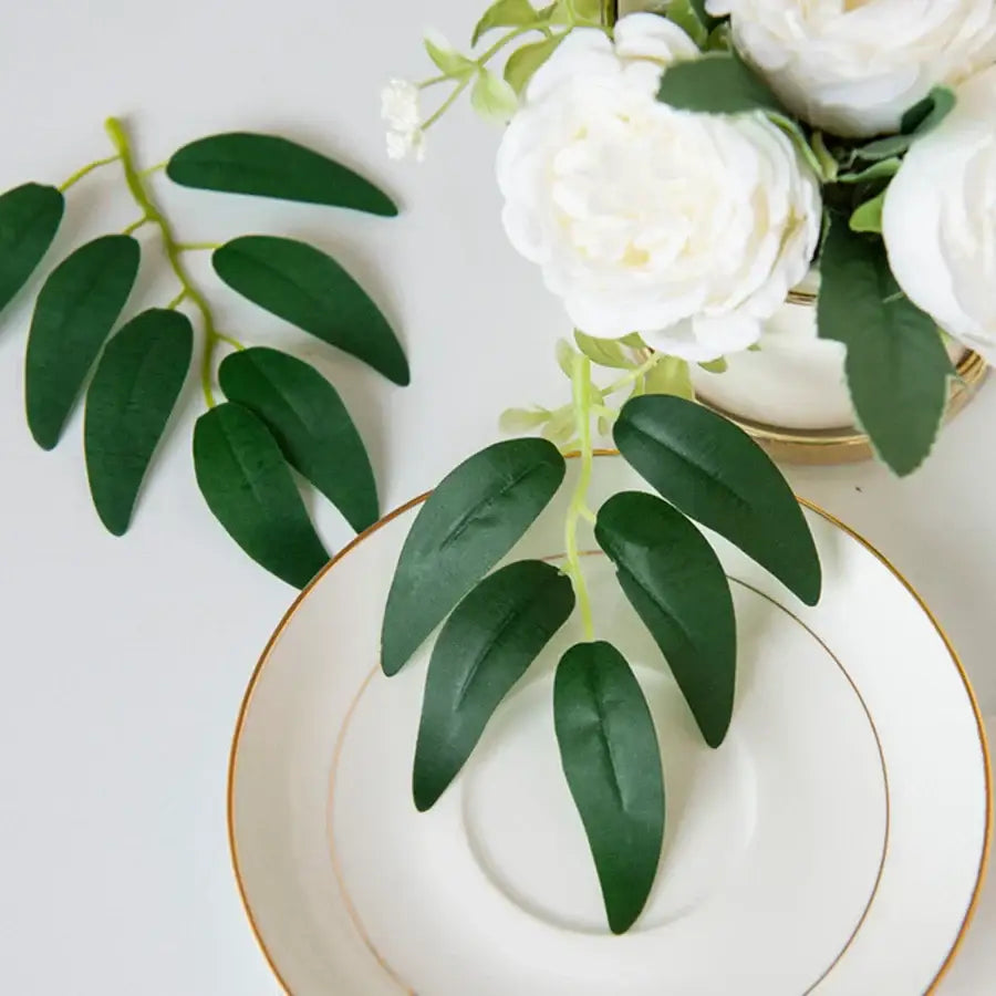 White artificial roses with dark green silk willow leaves in a gold-rimmed vase for wedding and home decor