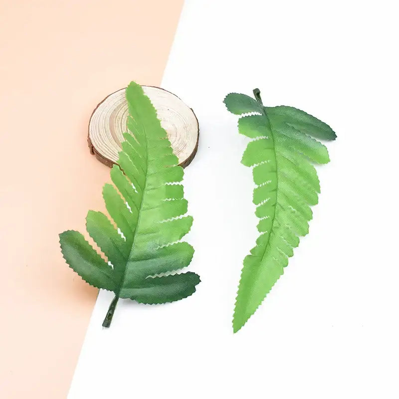 Two artificial green fern leaves with detailed veining and textured surfaces on a wooden slice for decorbites fake leaves decor