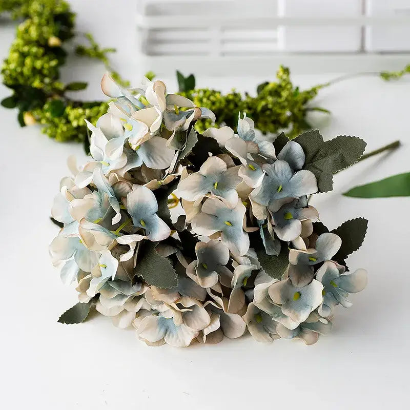 A delicate decorbites hydrangea branch decor with realistic soft blue and cream petals and dark green leaves for wedding decor