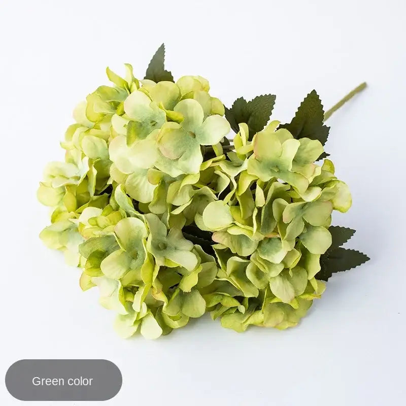 A cluster of artificial green hydrangea flowers with layered petals and dark leaves in decorbites hydrangea branch decor
