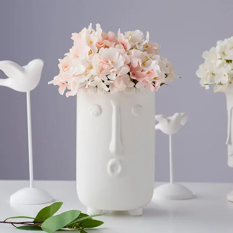 White ceramic vase with stylized face holding realistic pink and white decorbites hydrangea branch decor