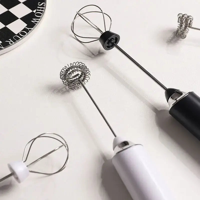 Two rechargeable electric milk frother mixers with sleek black and white handles and silver and black wire whisk attachments