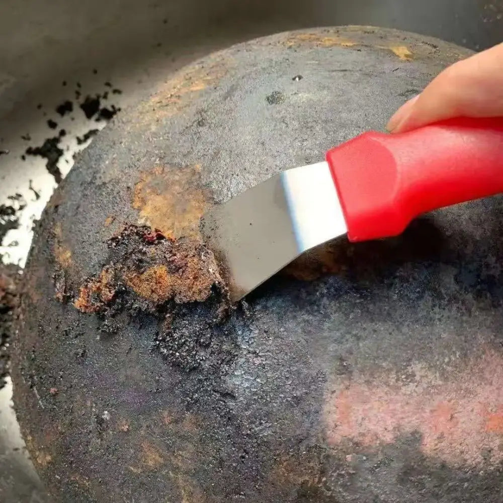 Red and black stainless steel ice remover tool with red handle scraping burnt residue from dark frying pan decorbites ice remover