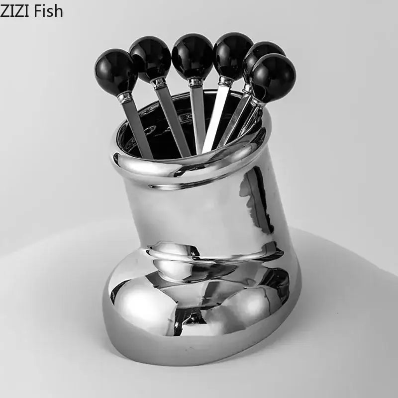 Red ceramic boot desk organizer box with shiny chrome spoon rest holding six black spherical-handled spoons