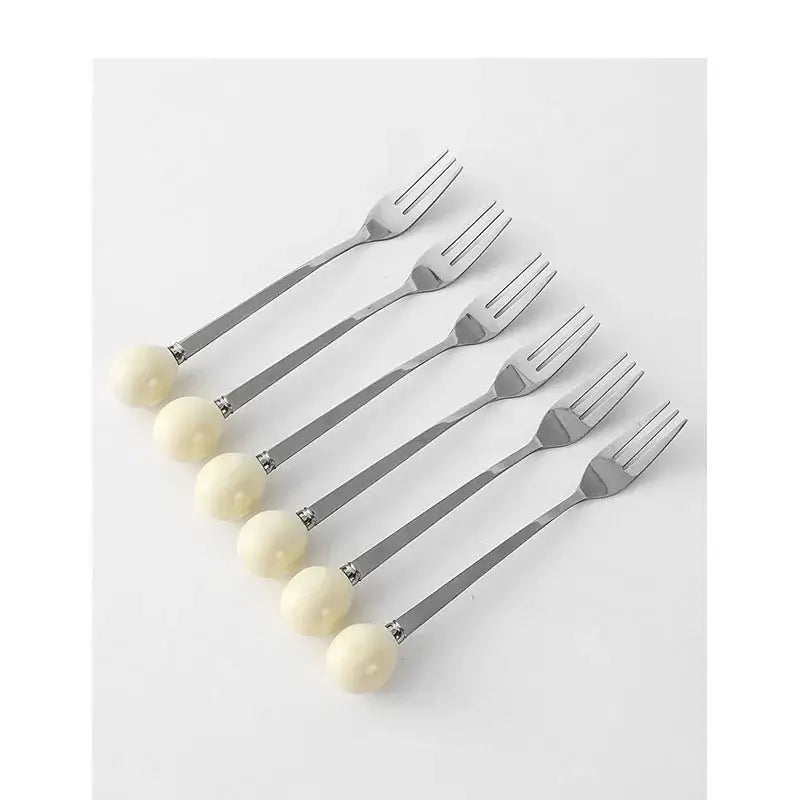 Set of six elegant stainless steel dessert forks with smooth ivory handles displayed with a red ceramic desk organizer box