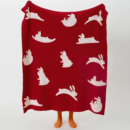 A cozy red knitted throw blanket with decorbites lively rabbit pattern featuring white rabbits for bedroom decor