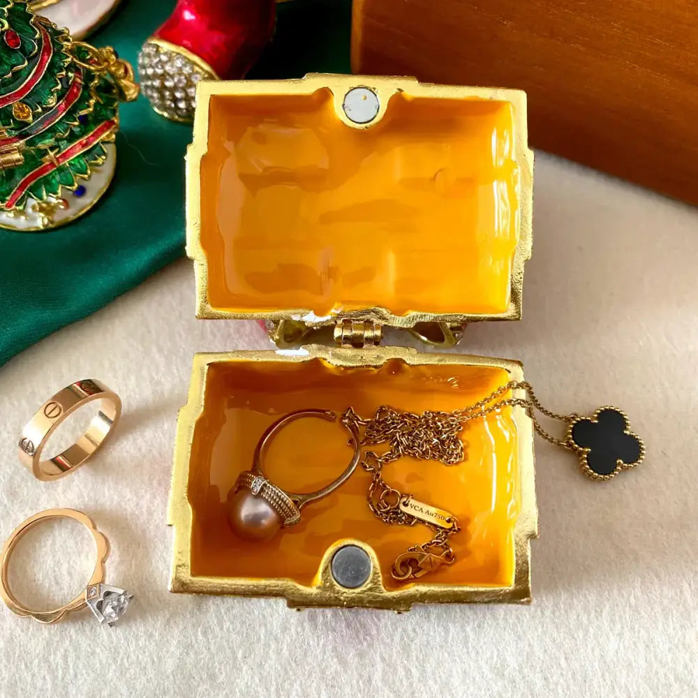 Gold-trimmed red and white bow jewelry trinket box with vibrant orange interior holding delicate pearl ring and pendant
