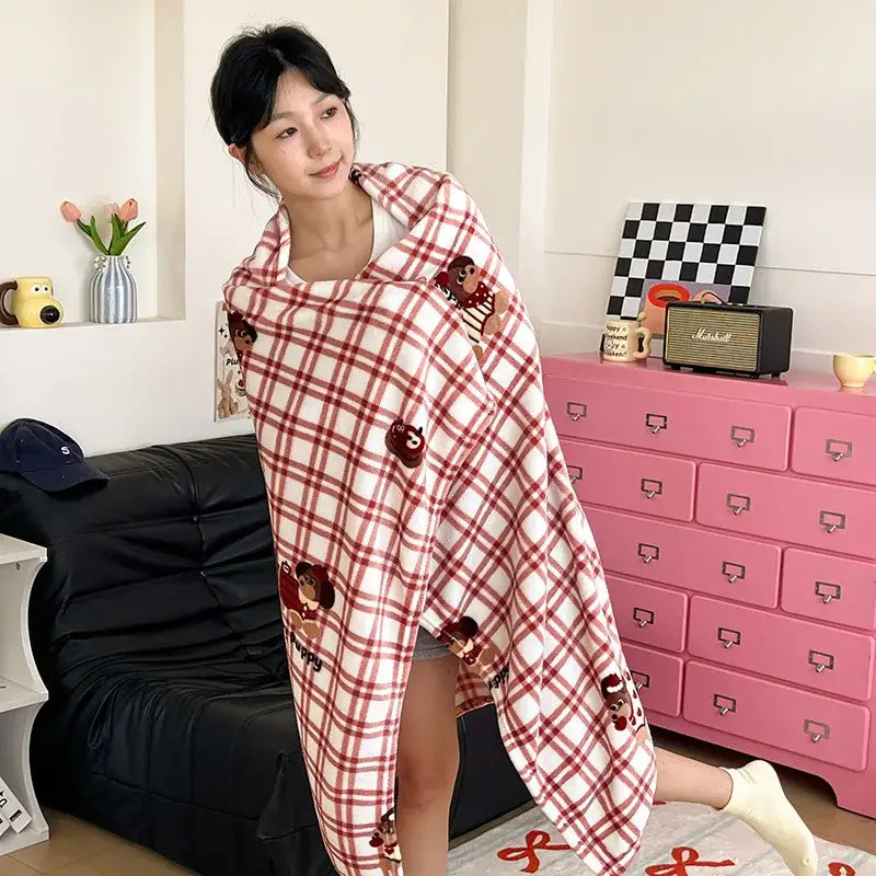 A cozy red and white plaid velvet printed blanket with embroidered cartoon bear patches draped over a woman’s shoulders
