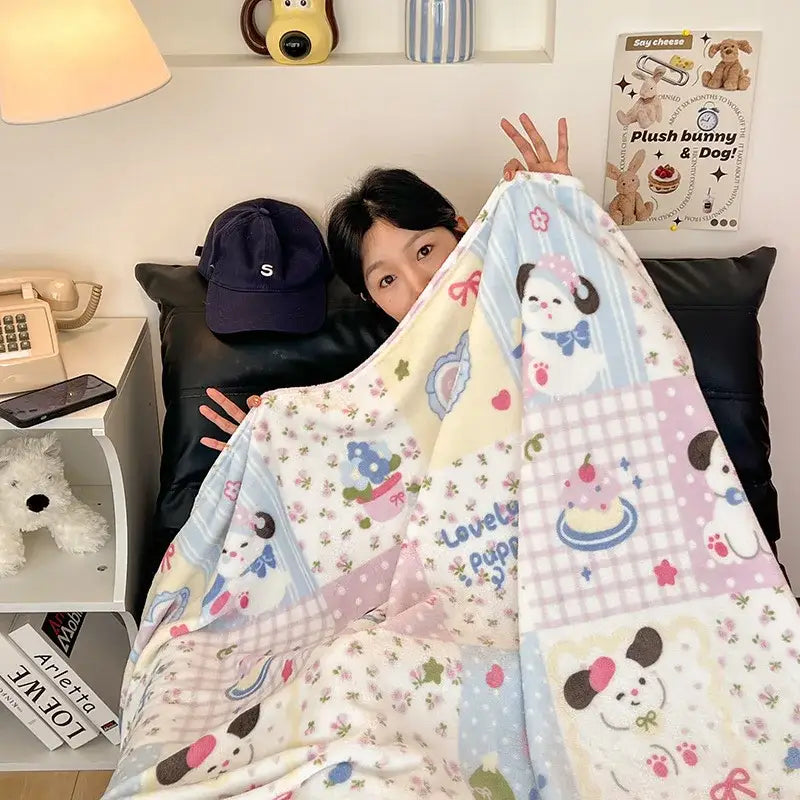 A soft pastel velvet printed blanket with playful patchwork of cartoon bunnies and cupcakes in blue pink and white