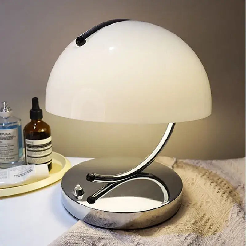 A sleek white dome-shaped decorbites glass table lamp with a chrome base and curved stem for stylish bedroom use