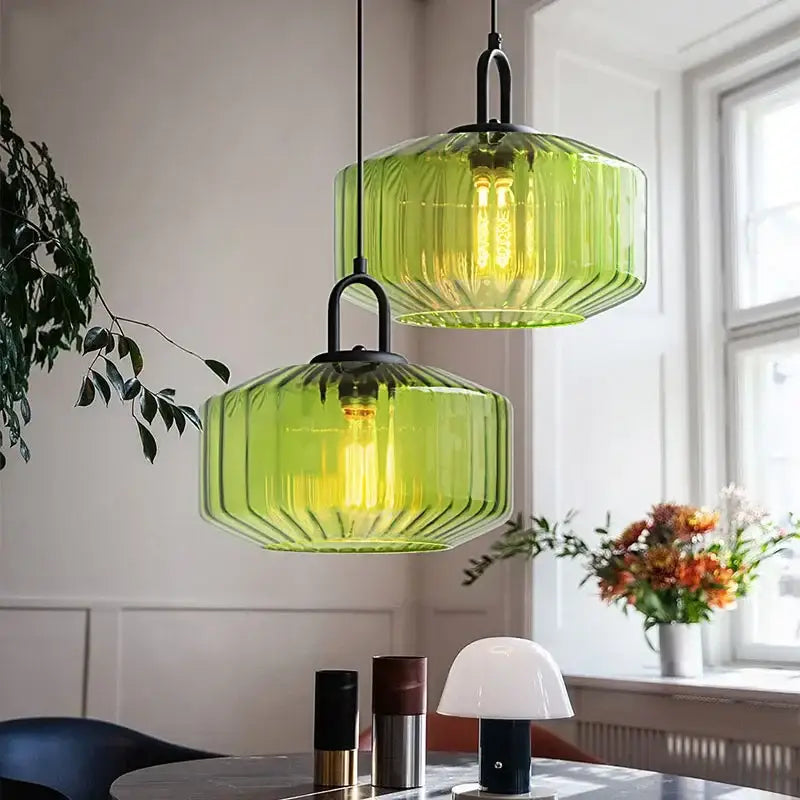 Two green ribbed glass pendant lights with black metal fixtures in a retro amber and green color glass dining chandelier