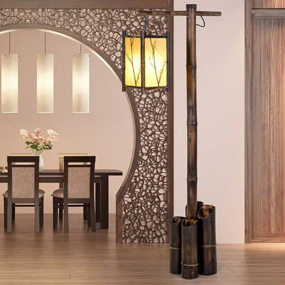 A rustic bamboo weave floor lamp with a warm amber-lit lantern featuring delicate branch cutouts for zen living rooms