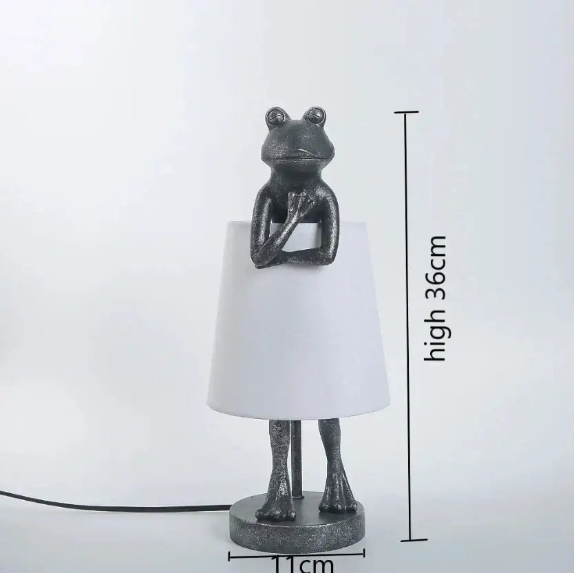 A retro black frog resin desk lamp features a metallic frog base with crossed arms and a sleek white shade for bedroom lighting