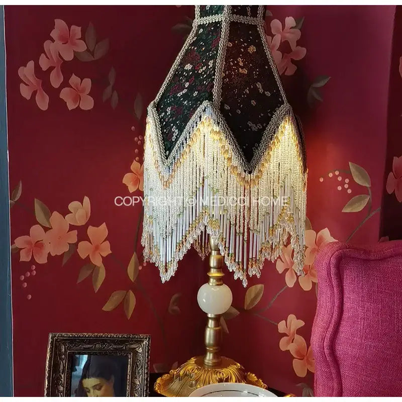 An ornate retro table lamp with a dark green roses retro beaded fringe shade on an elegant brass base