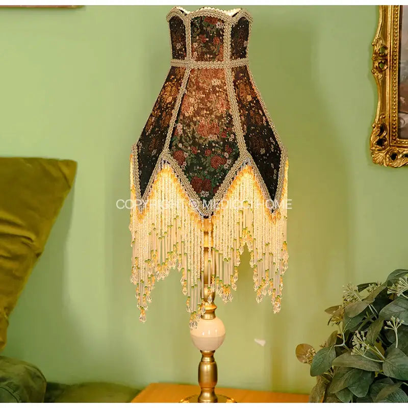 An ornate retro table lamp with dark floral black and green roses fabric shade and gold trimmed beaded fringe