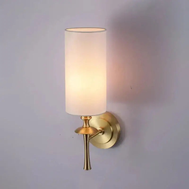 A warm-toned fabric cylindrical lampshade on a brass wall lamp with a black metal decorbites brass wall sconce base