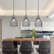 Three black metal decorbites cage bell pendant lights hang above a wooden dining table as pendant light decor