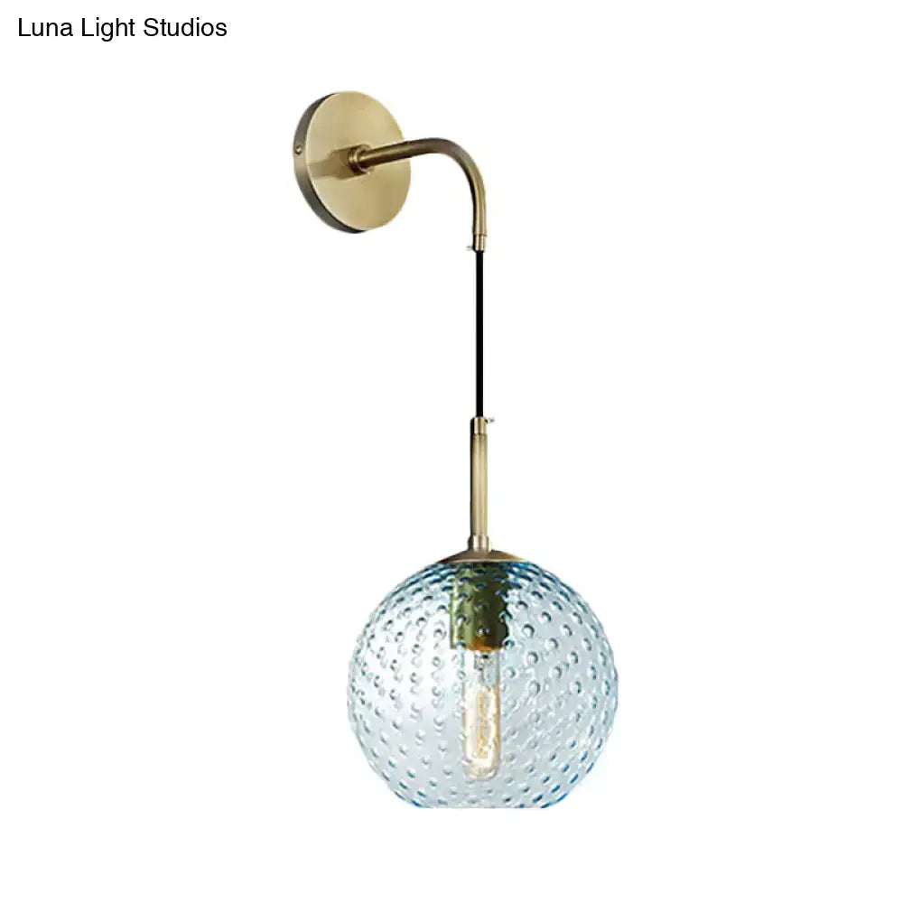 Retro blue glass globe wall lamp with textured bubble surface hanging from brass arm in pink yellow blue light