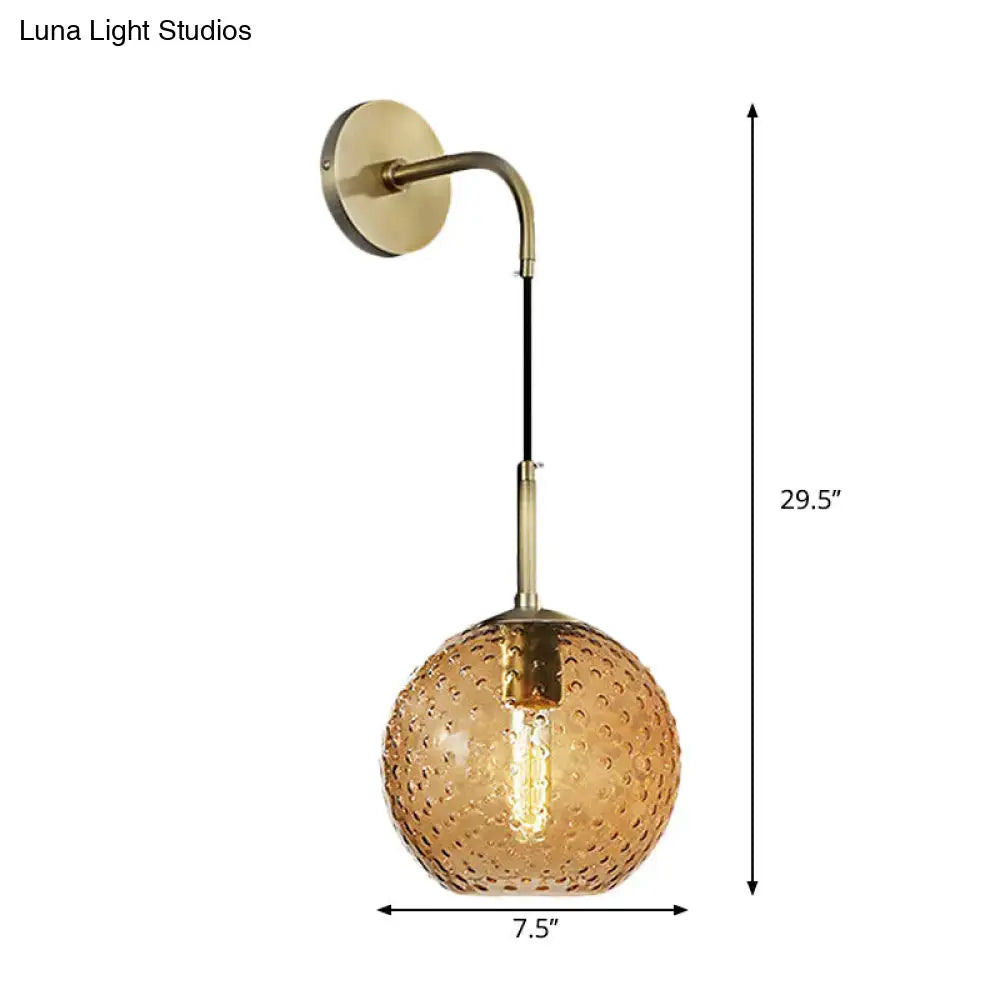 A brass-finished wall sconce with textured amber glass globe and exposed filament bulb for pink yellow blue lighting