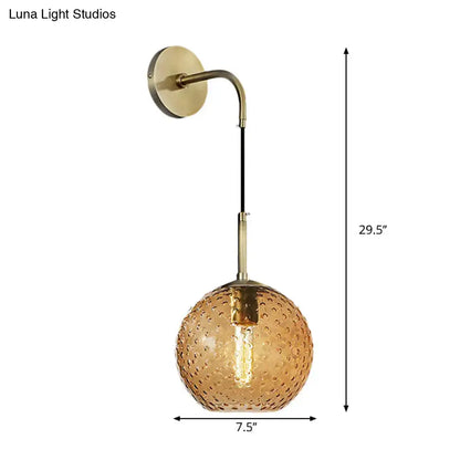 A brass-finished wall sconce with textured amber glass globe and exposed filament bulb for pink yellow blue lighting