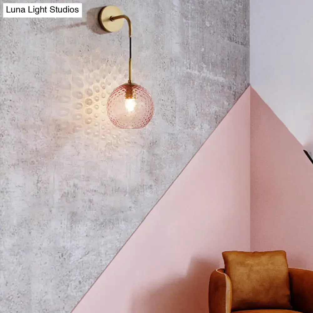 A delicate pink glass globe pendant light with brass finish on a curved arm for retro pink yellow blue decor