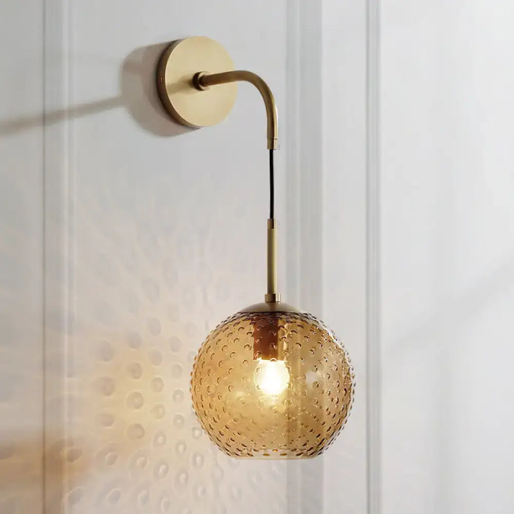 Gold-toned wall sconce with amber textured glass globe featuring pink yellow blue hues for bedroom lighting