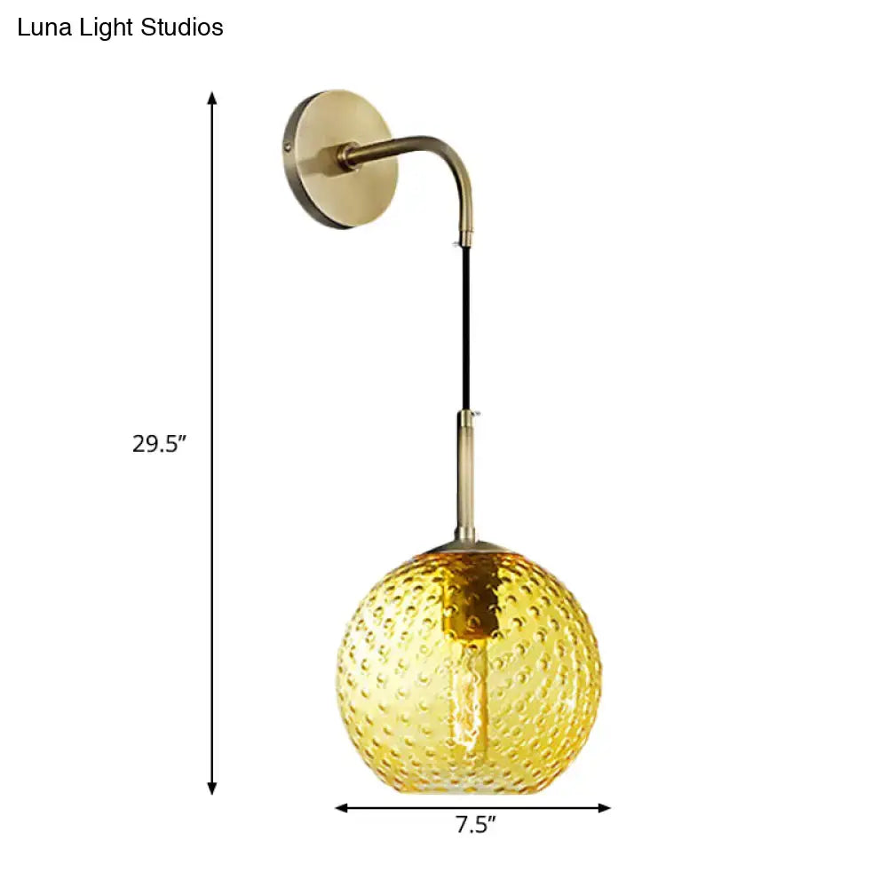 A golden-hued textured glass globe hangs from a brass arm in a retro pink yellow blue wall lamp for bedroom lighting