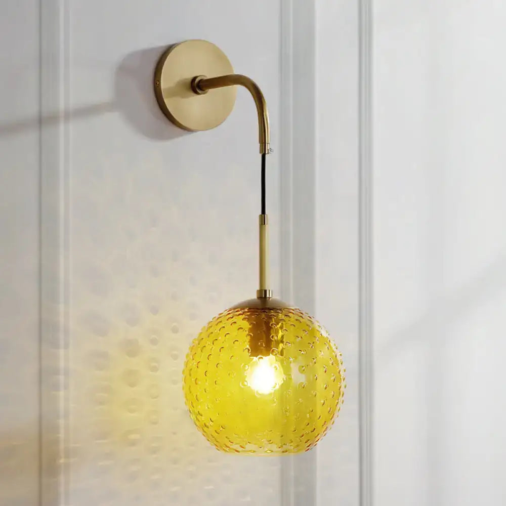 A warm yellow textured glass globe hangs from a curved brass arm in a retro pink yellow blue wall lamp fixture