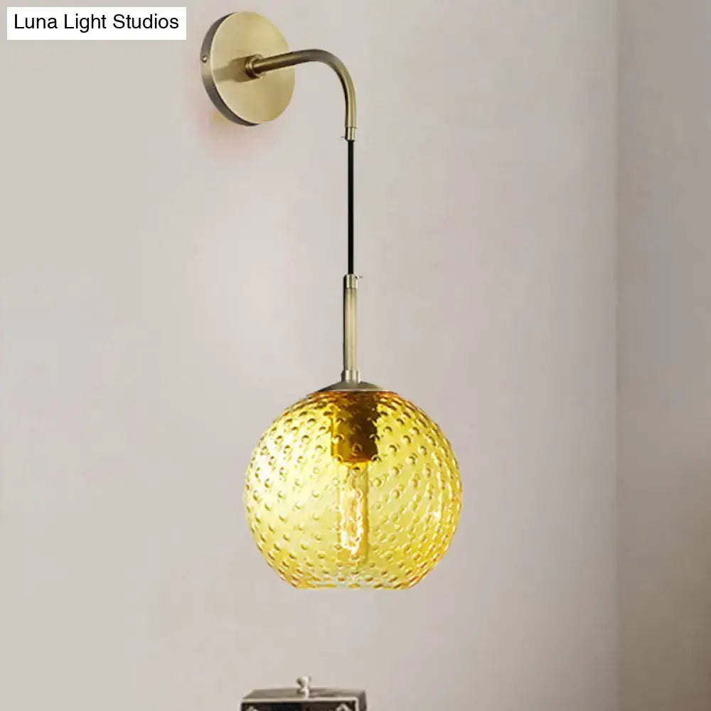 A warm amber glass globe pendant light with textured bubble surface and brass hardware for pink yellow blue decor