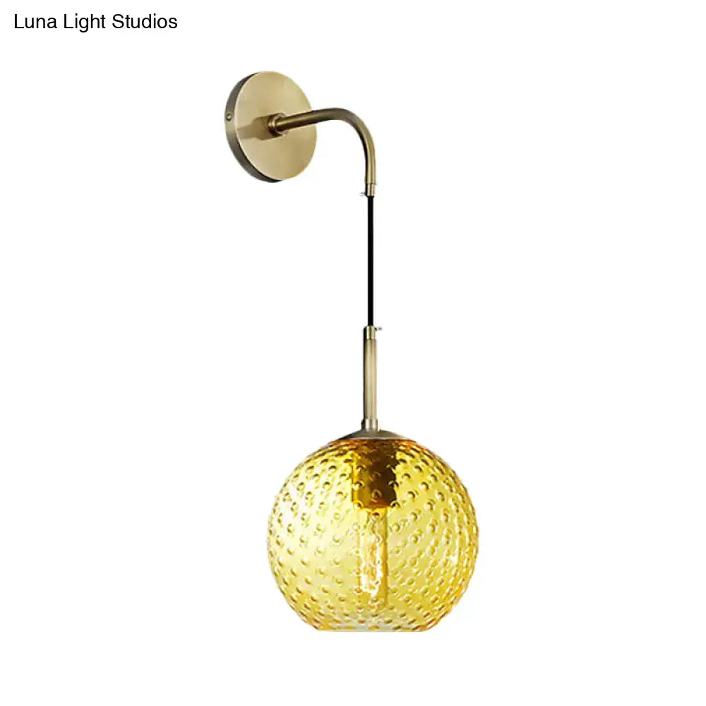 A warm amber glass globe pendant light with textured bubbles and a curved brass arm for pink yellow blue decor