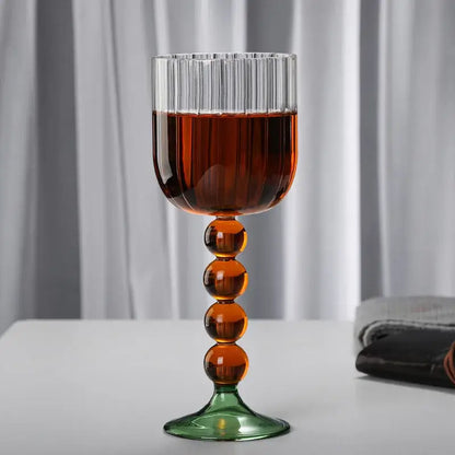 A tall elegant wine glass twister with clear ribbed bowl amber glass twister stem and green base for dining room use