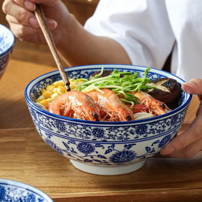 A white retro ceramic soup noodle bowl with blue floral patterns filled with vibrant seafood noodles