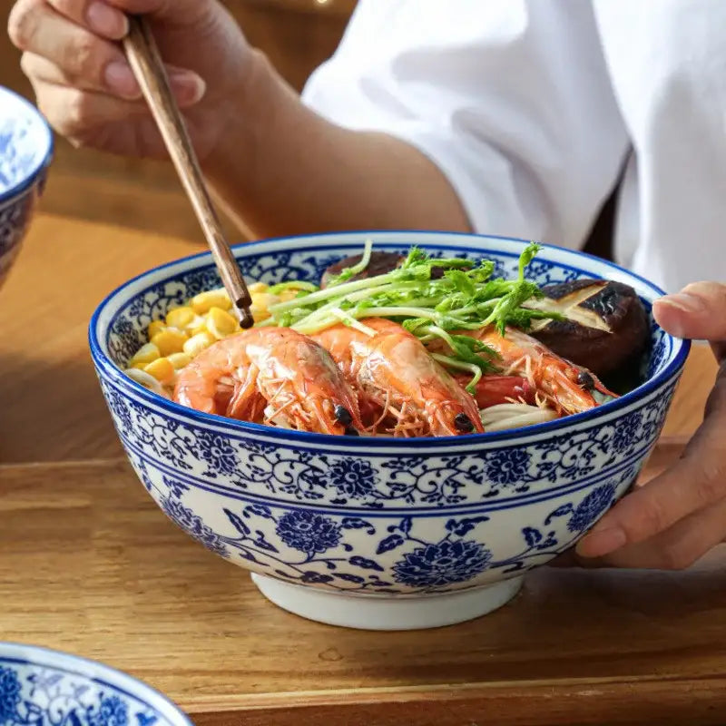 A white retro ceramic soup noodle bowl with blue floral patterns filled with vibrant seafood noodles