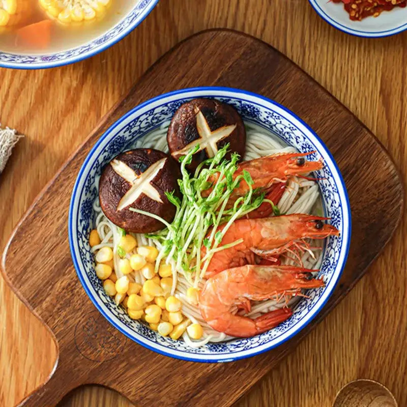 Blue and white white retro ceramic soup noodle bowl with floral patterns filled with shrimp noodles corn and mushrooms