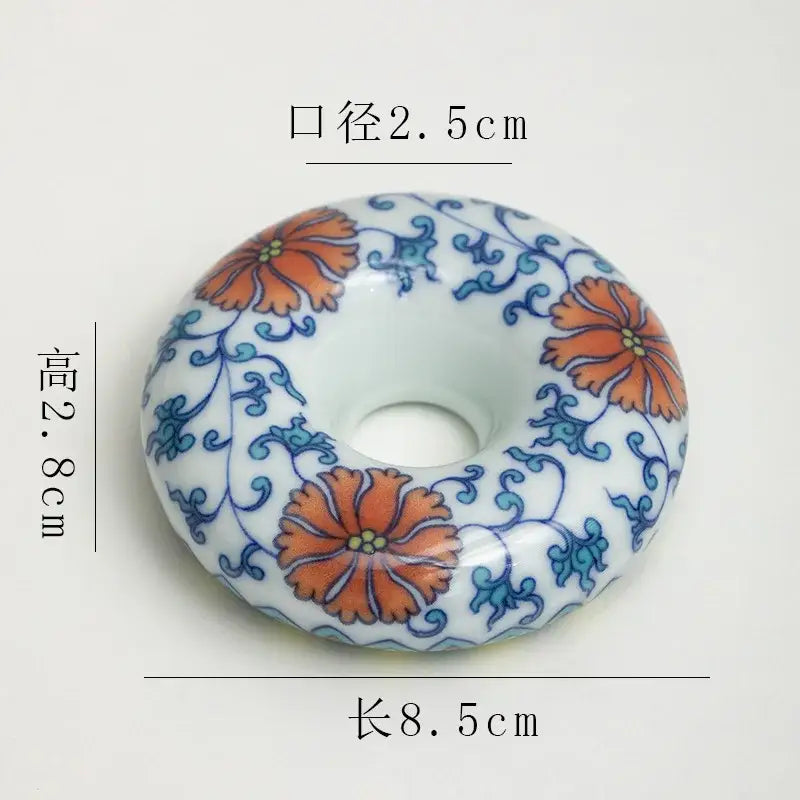 A white ceramic donut-shaped ornament with hand-painted orange and blue floral patterns in a teacup tray set