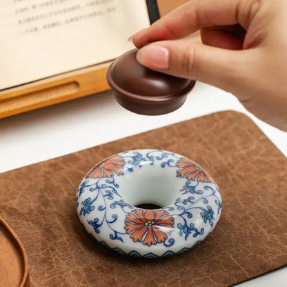 A ceramic donut-shaped incense burner with orange and blue floral patterns and wooden lid included in a teacup tray set