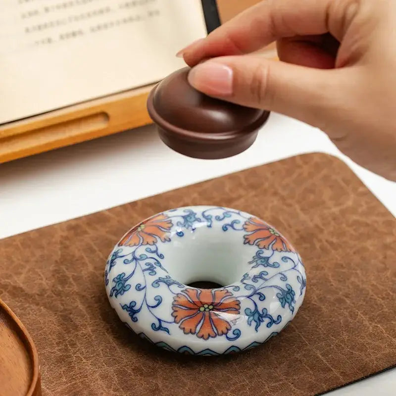 A ceramic donut-shaped incense burner with orange and blue floral patterns and wooden lid included in a teacup tray set