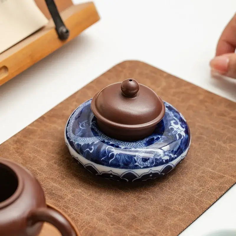 A traditional chinese-style ceramic incense burner with dark brown lid on a blue-and-white porcelain teacup tray set