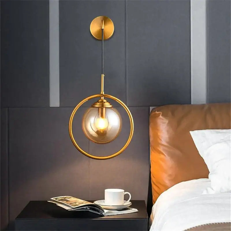 Gold-toned retro brass decorbites glass ball wall lamp with circular frame and clear glass globe housing exposed bulb