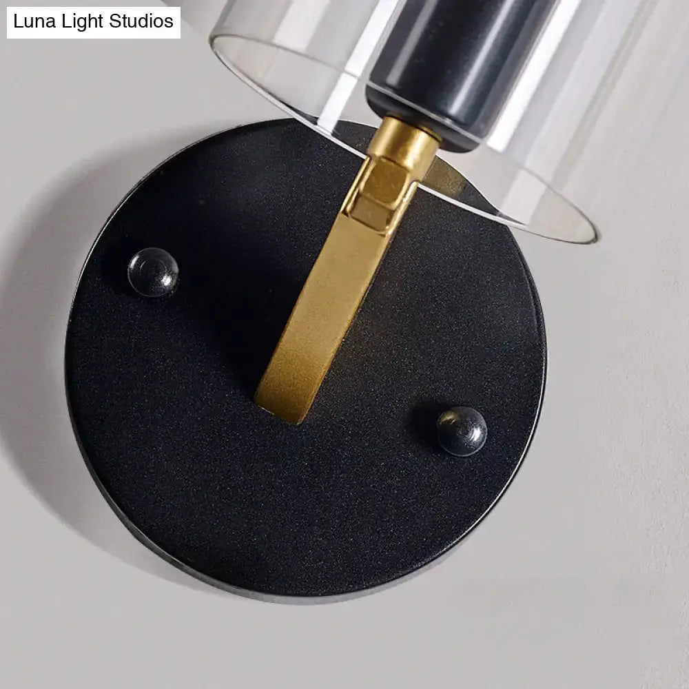 Black circular wall light with a gold-toned metal arm and transparent glass sconce for bedroom use
