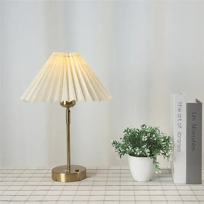 Cream-colored pleated table lamp with brass-finished metal base featuring decorbites adjustable pleated design