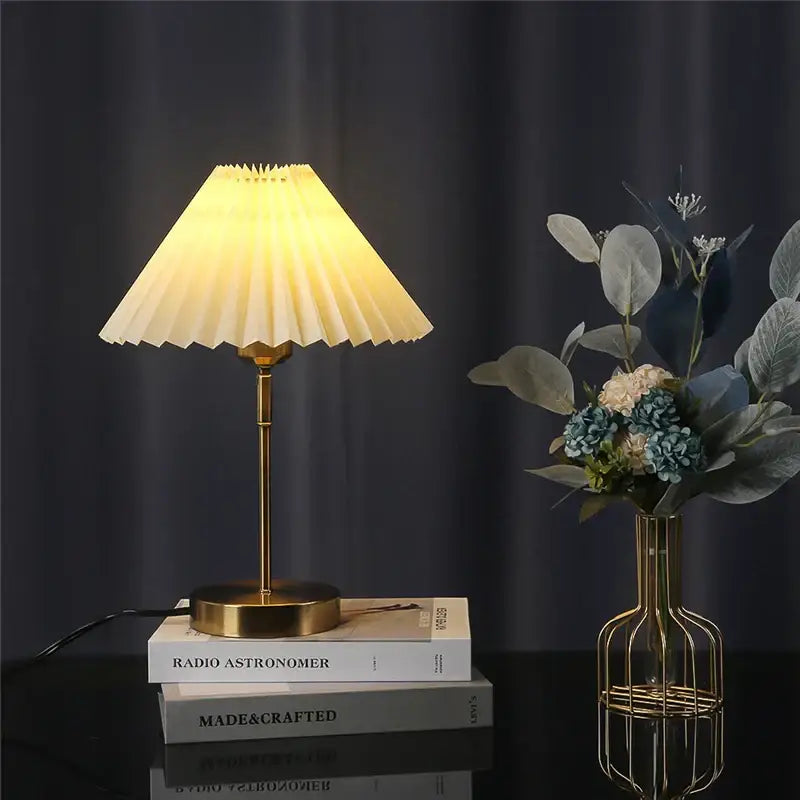 Retro brass and cream adjustable pleated table lamp with warm-toned pleated shade on stacked books for bedroom light