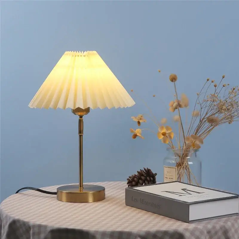 A warm-toned brass adjustable pleated table lamp with a cream off-white fabric shade for bedroom lighting