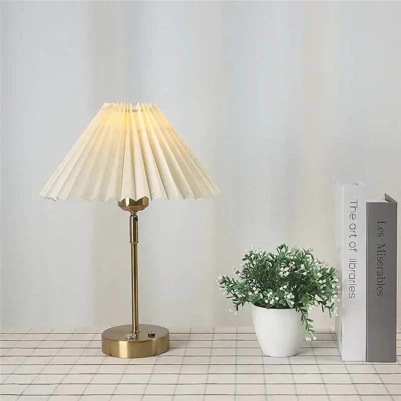 Cream-colored pleated table lamp with brass-finished base and stem featuring an adjustable pleated design for bedroom use