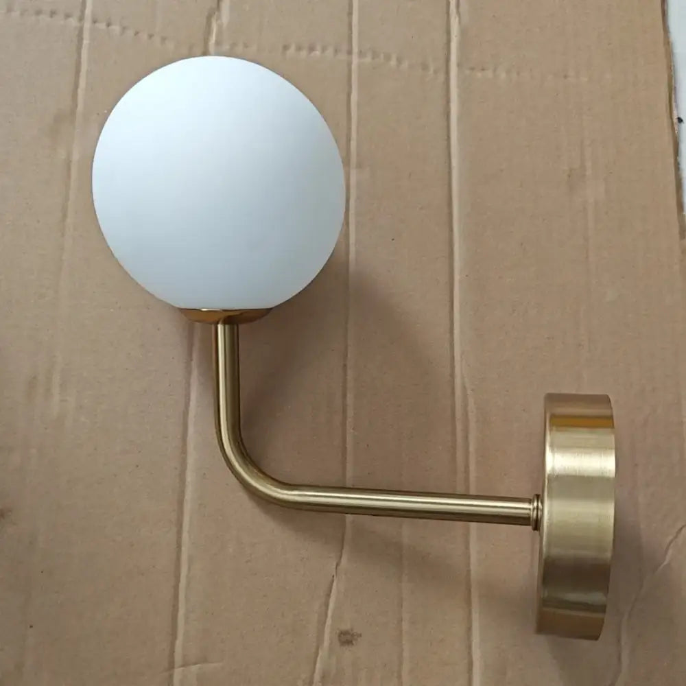 A sleek retro brass wall lamp with a curved brass finish and frosted white decorbites glass ball shade