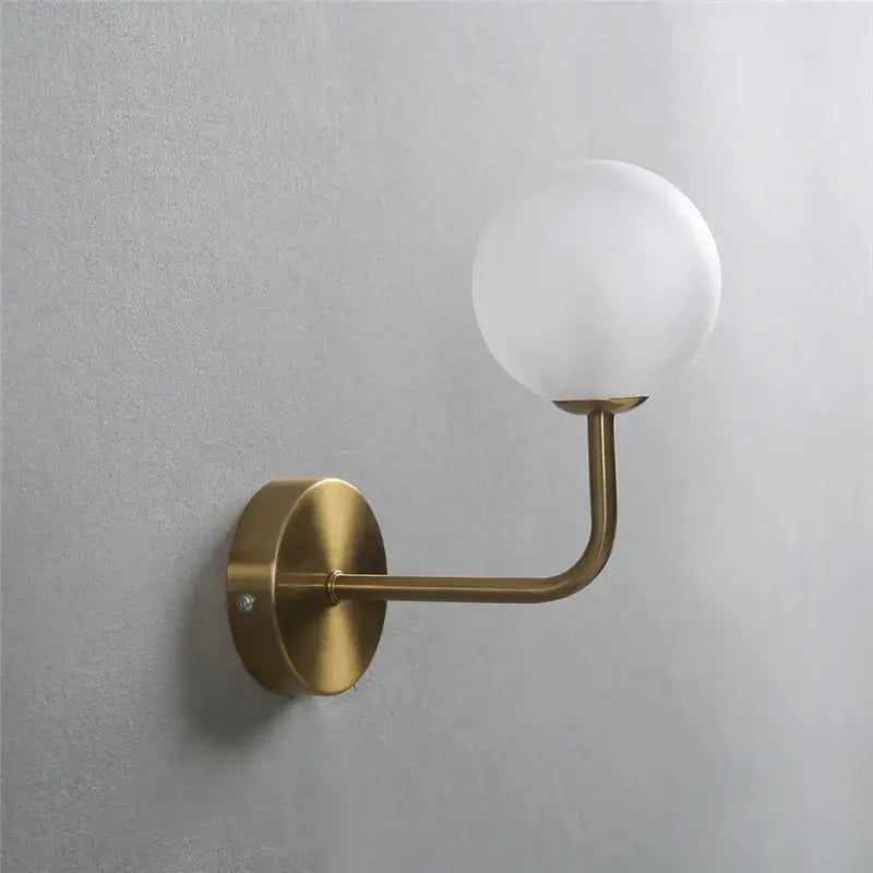 A sleek brass wall lamp with a curved arm and frosted glass ball shade perfect for bedroom decorbites glass ball